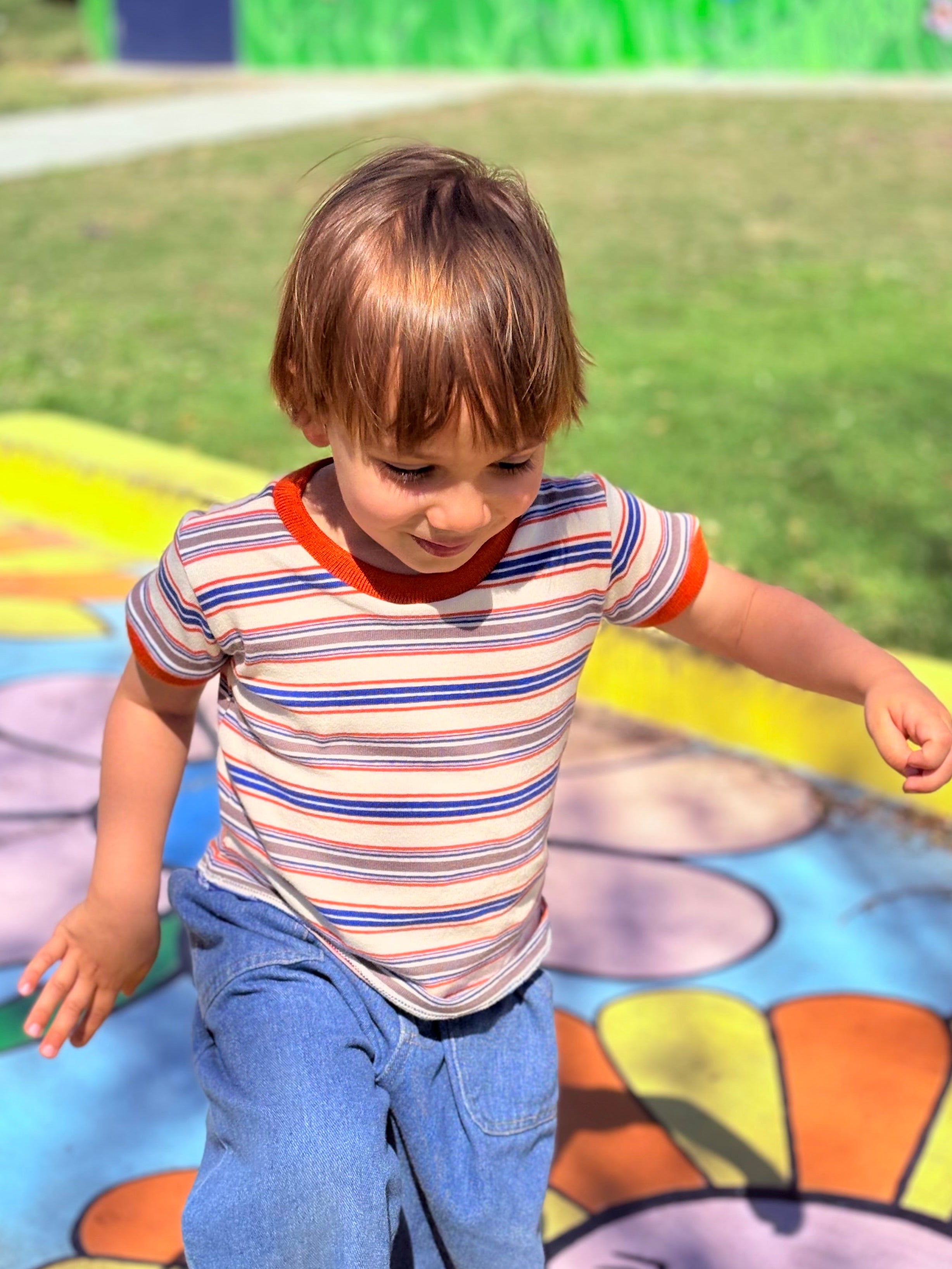 child playing in colorful playground wearing 80s style striped ringer tee
