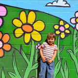 Child standing in front of a colorful mural of flowers and greenery wearing 80s ringer tee