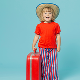 child wearing cool outfit with red shirt, vintage style wide leg striped pants, holding a red suitcase and a blue background
