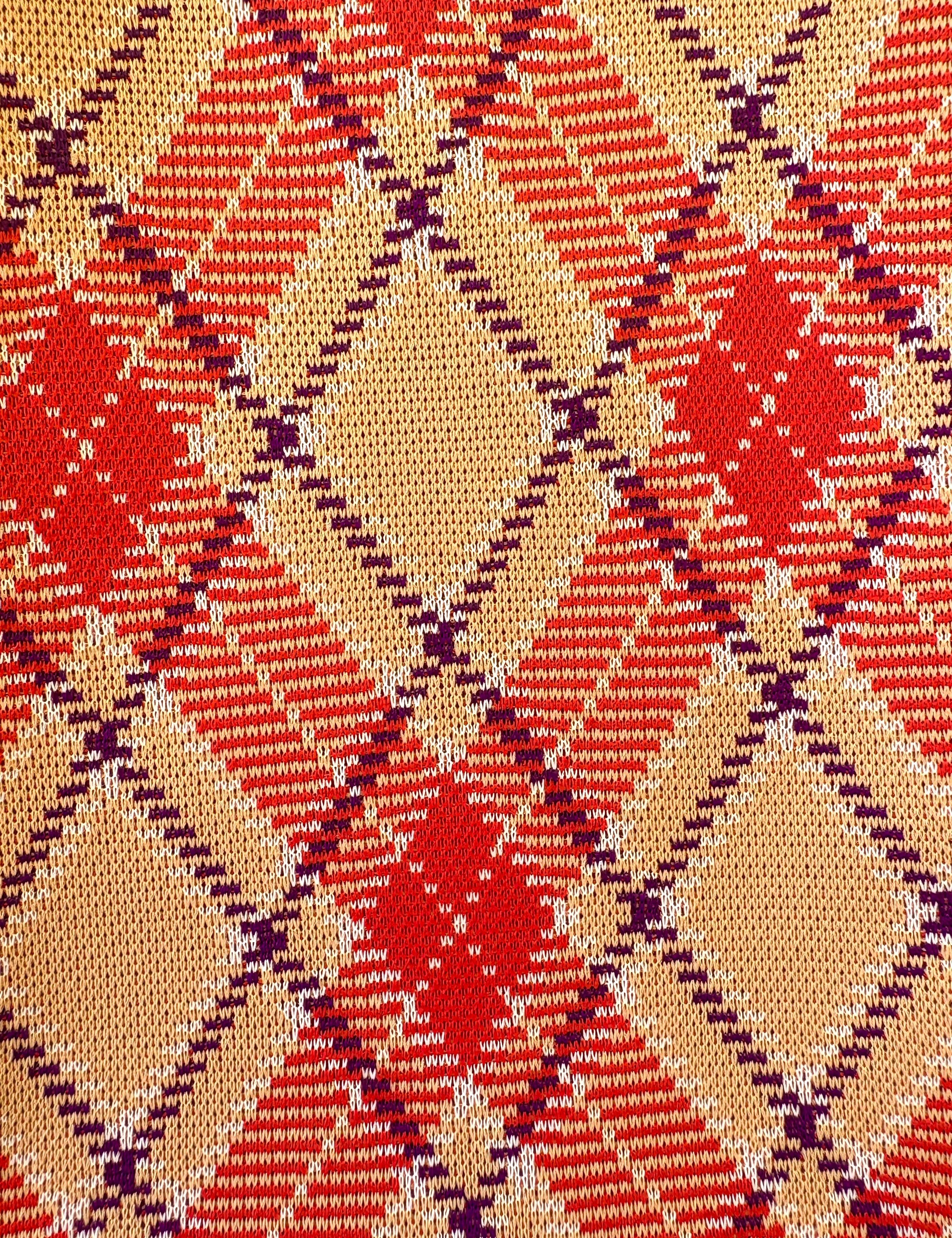 Close-up of a patterned fabric with red, beige, and purple colors.