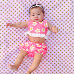 Baby wearing a pink flower power groovy  floral outfit lying on a pink floral blanket