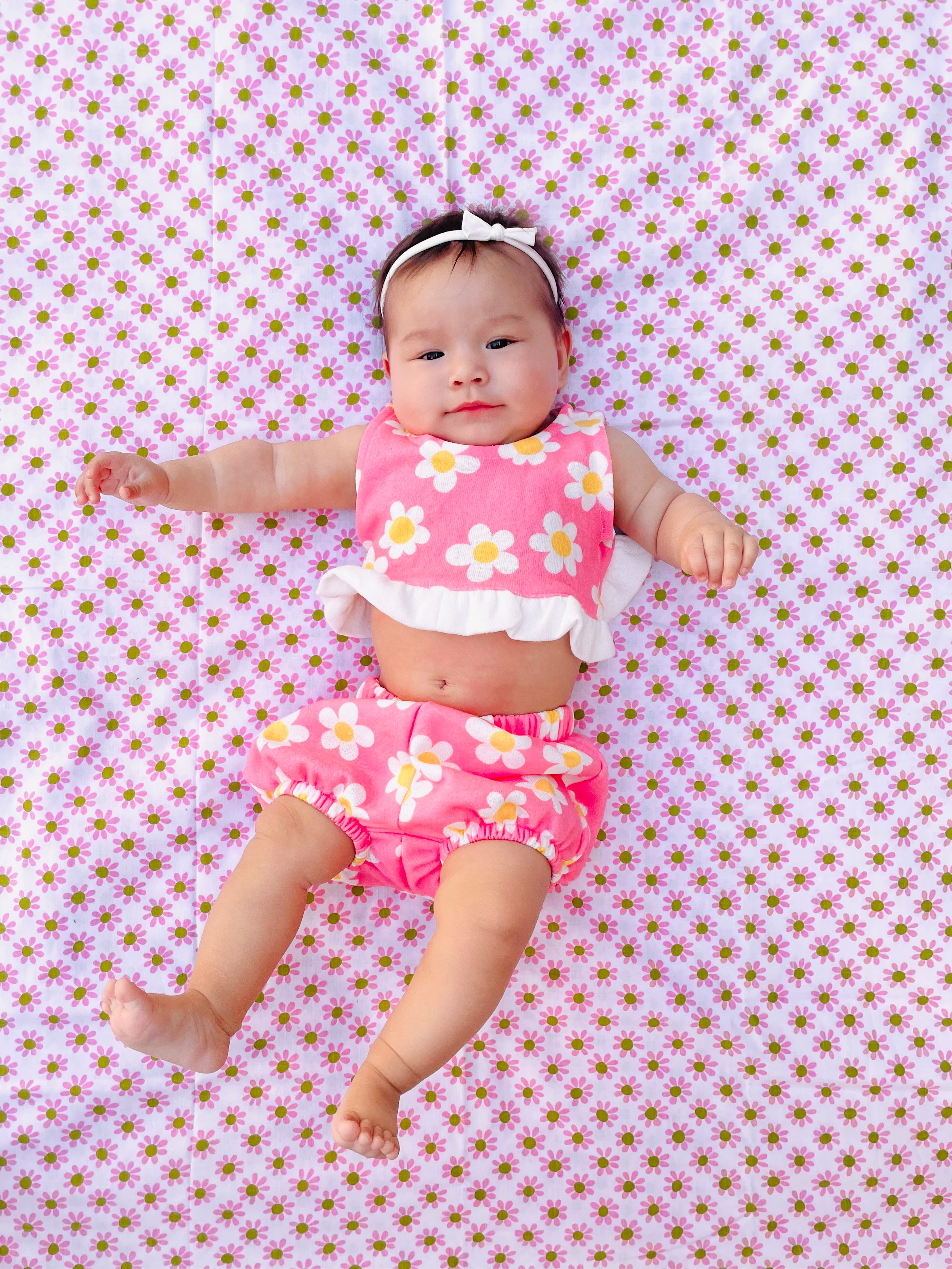 Baby wearing a pink flower power groovy  floral outfit lying on a pink floral blanket