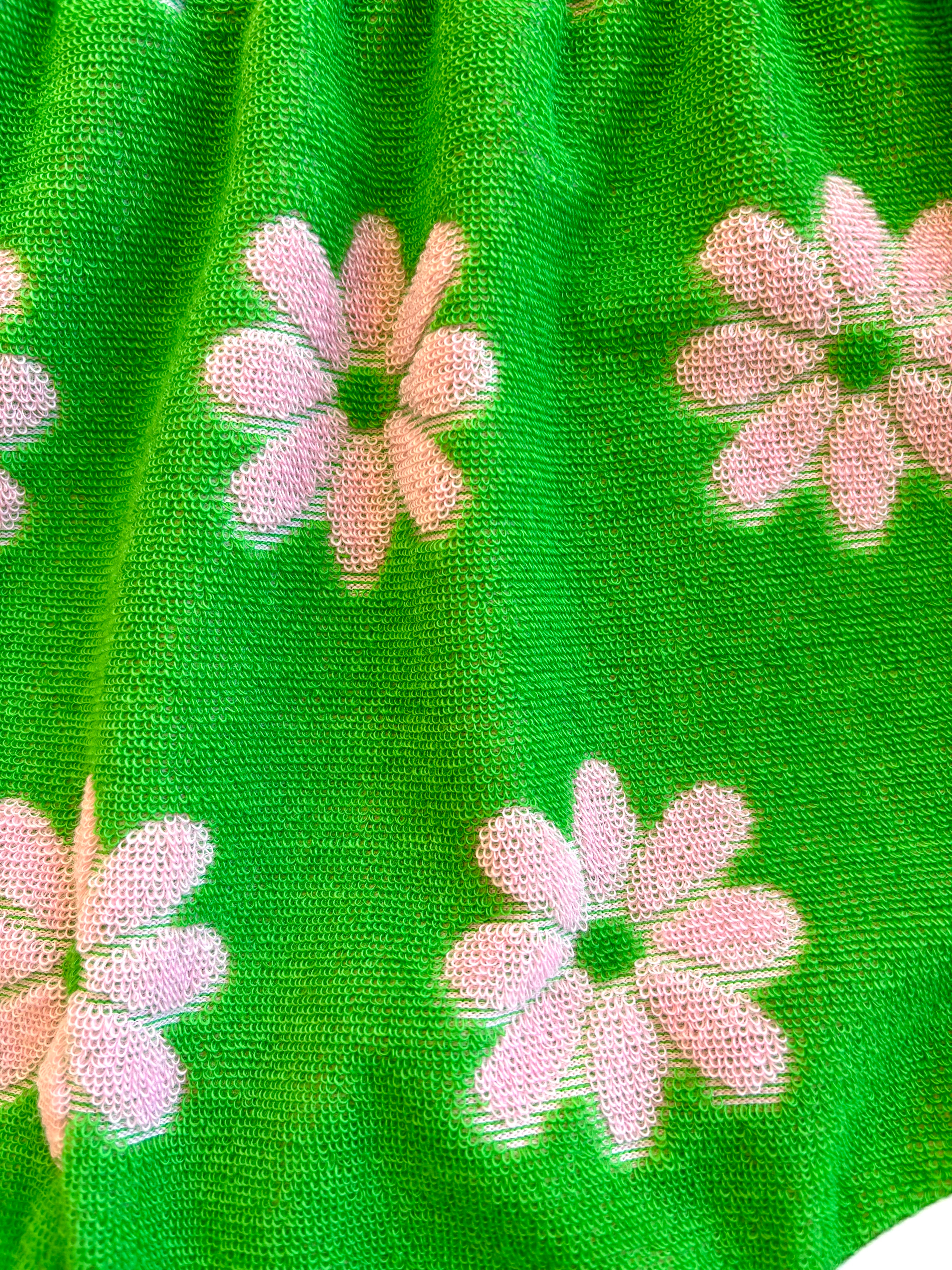 Close-up of green flower power Terry cloth fabric with pink floral patterns