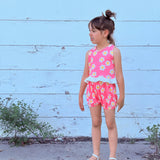 young girl wearing colorful stylish pink groovy floral outfit against white wall 