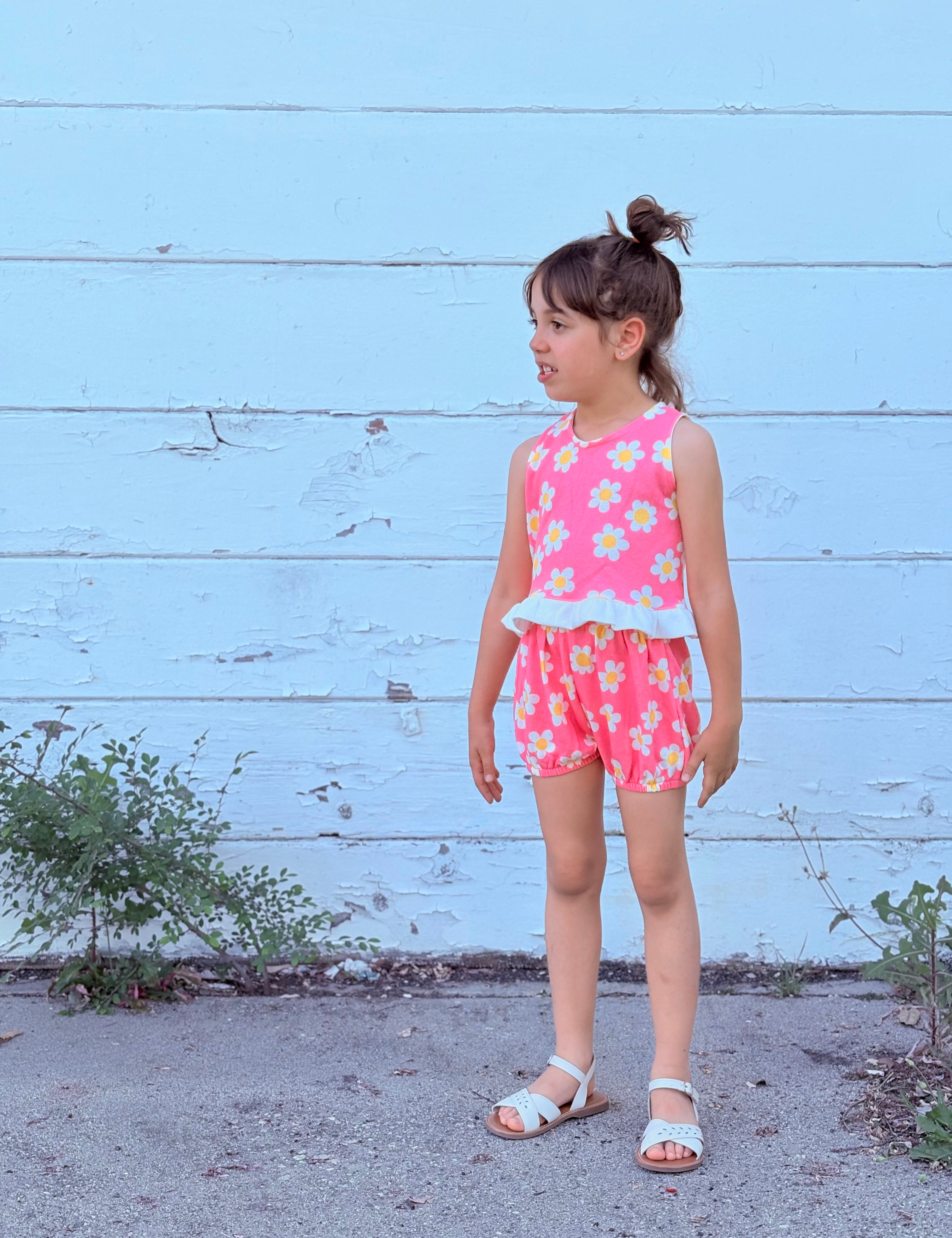 young girl wearing colorful stylish pink groovy floral outfit against white wall 