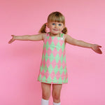 Young girl wearing cute vintage style green and pink patterned dress against a pink background