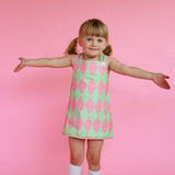 Young girl wearing cute vintage style green and pink patterned dress against a pink background