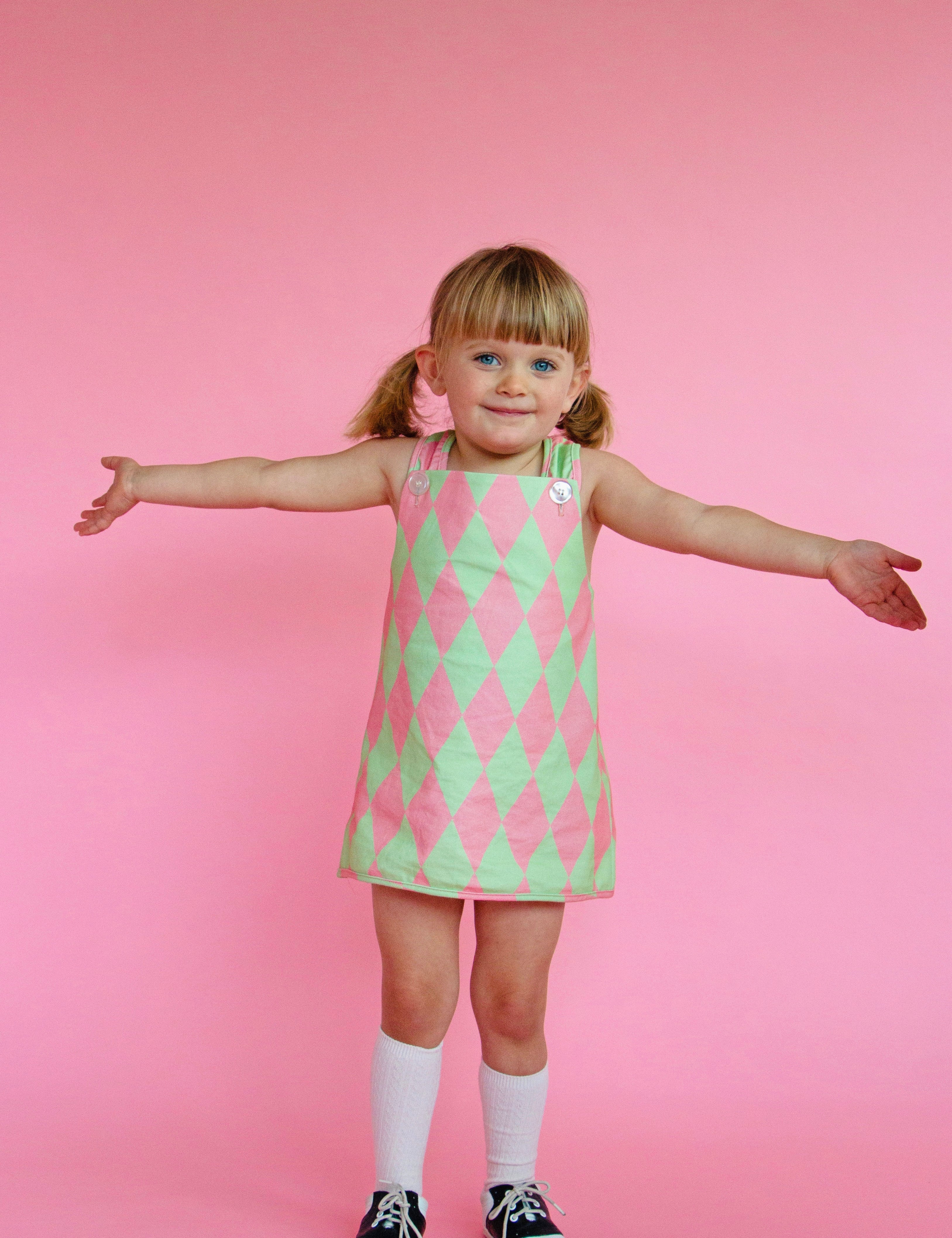 Young girl wearing cute vintage style green and pink patterned dress against a pink background