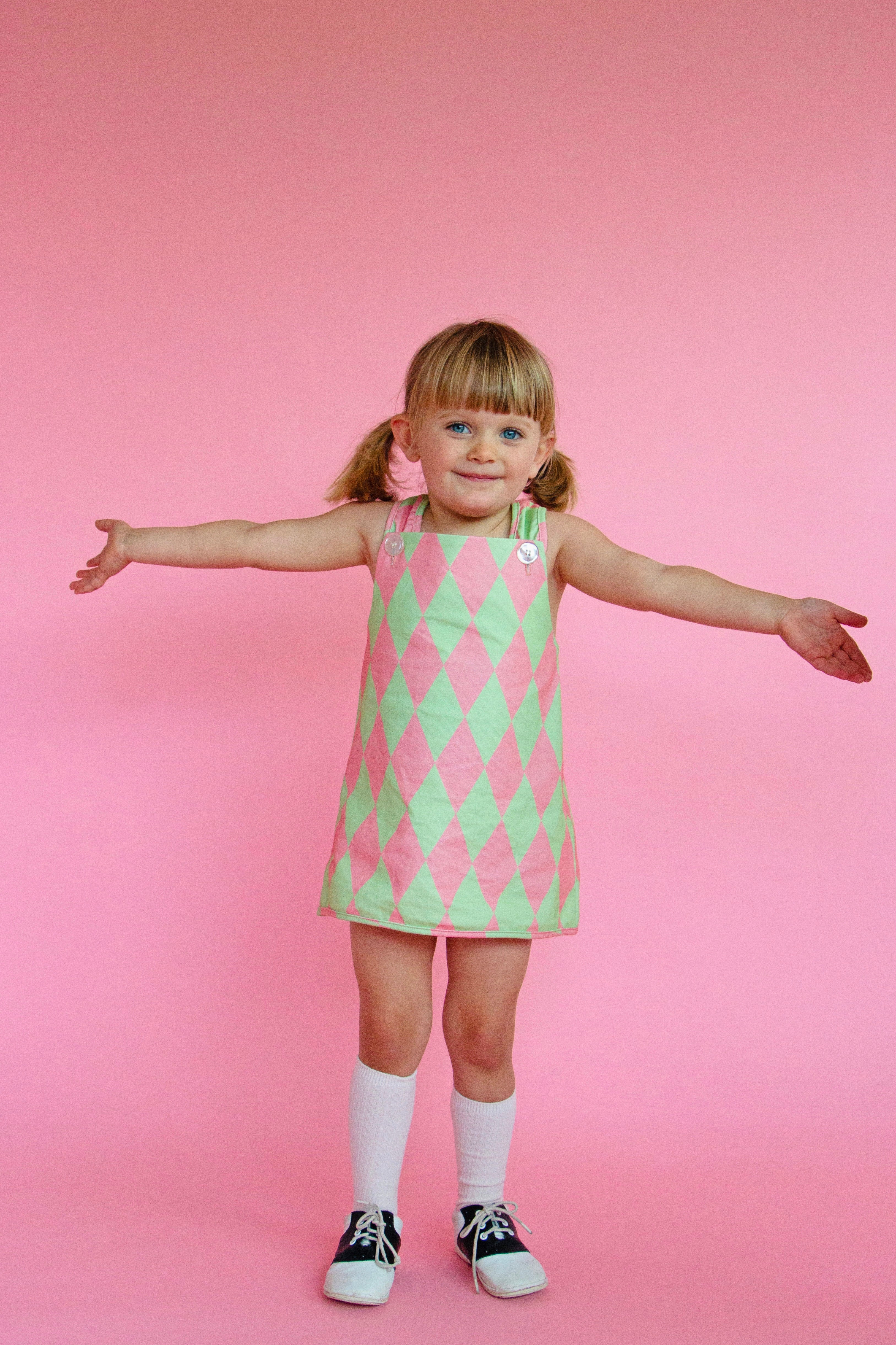 Young girl wearing cute vintage style green and pink patterned dress against a pink background