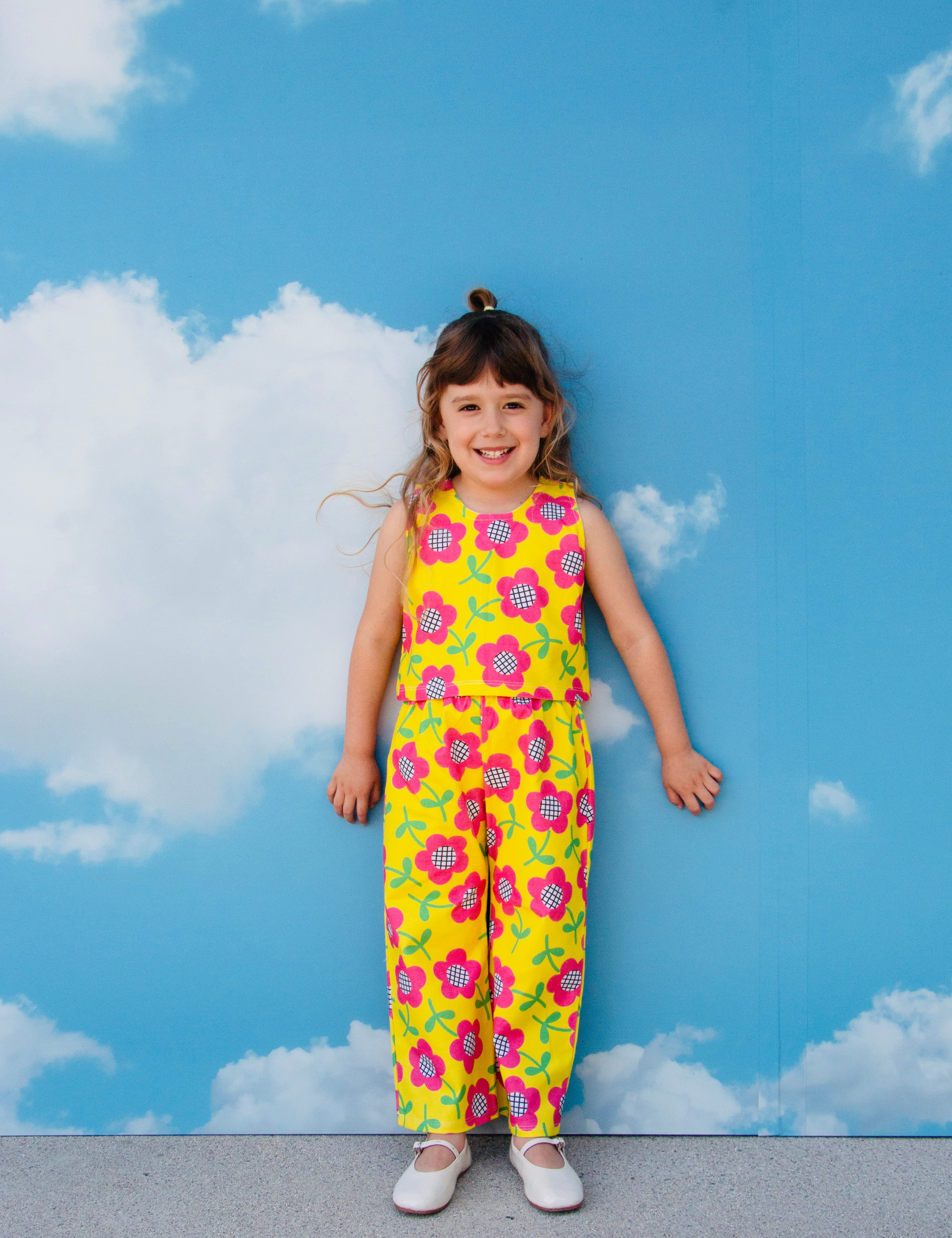 girl wearing cute retro pants set outfit with pink flowers on yellow background with sky backdrop