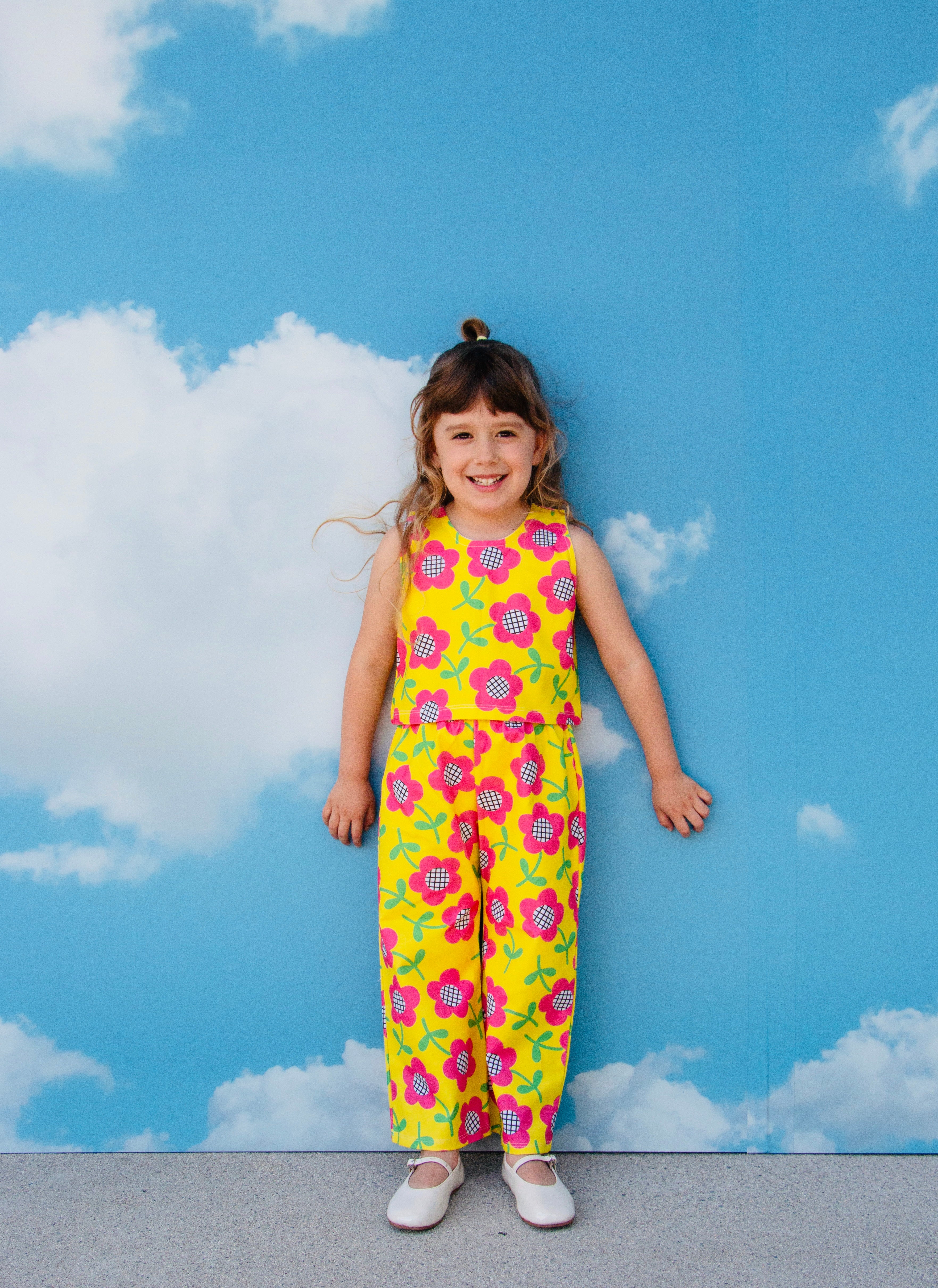 girl wearing cute retro pants set outfit with pink flowers on yellow background with sky backdrop