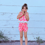 Young girl in a pink floral groovy flower power outfit standing against a light blue wooden wall.
