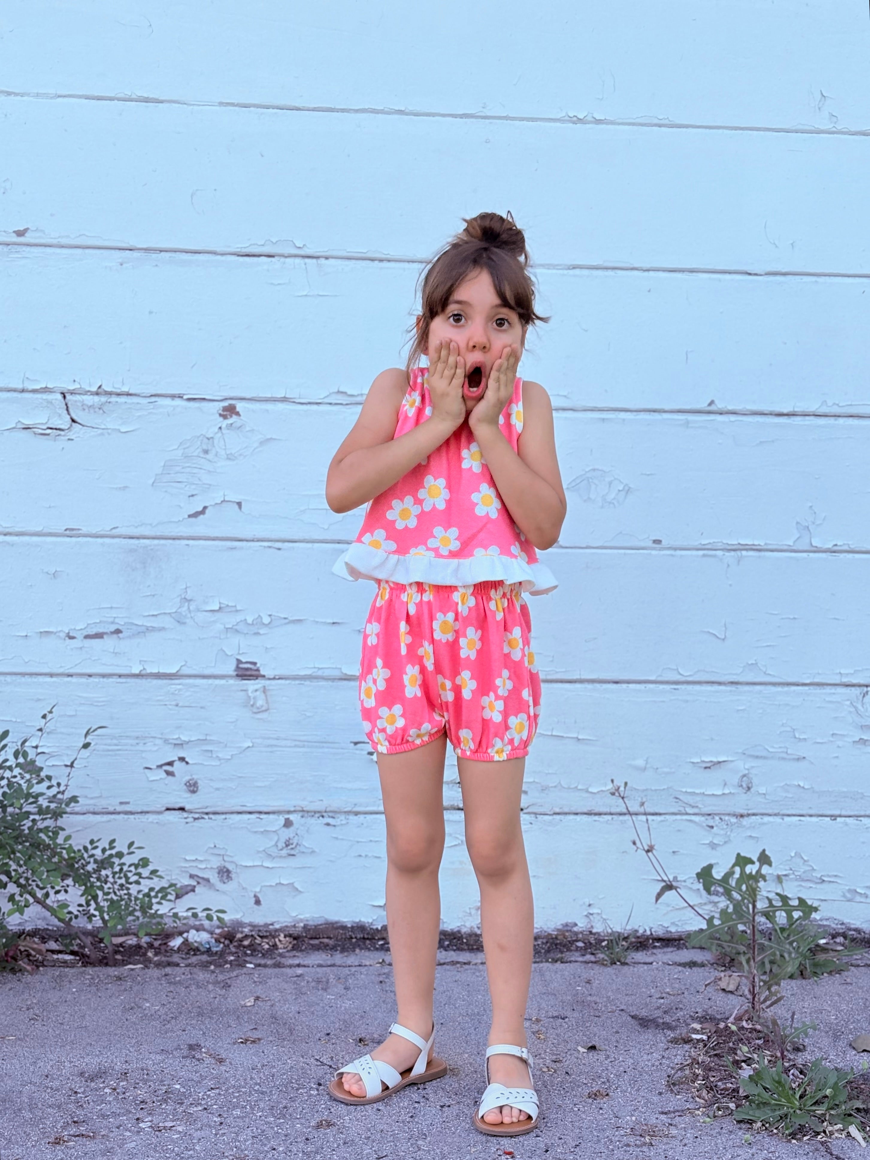 Young girl in a pink floral groovy flower power outfit standing against a light blue wooden wall.