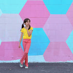 Girl wearing funky retro yellow top and red checkered pants standing in front of a colorful geometric-patterned wall.