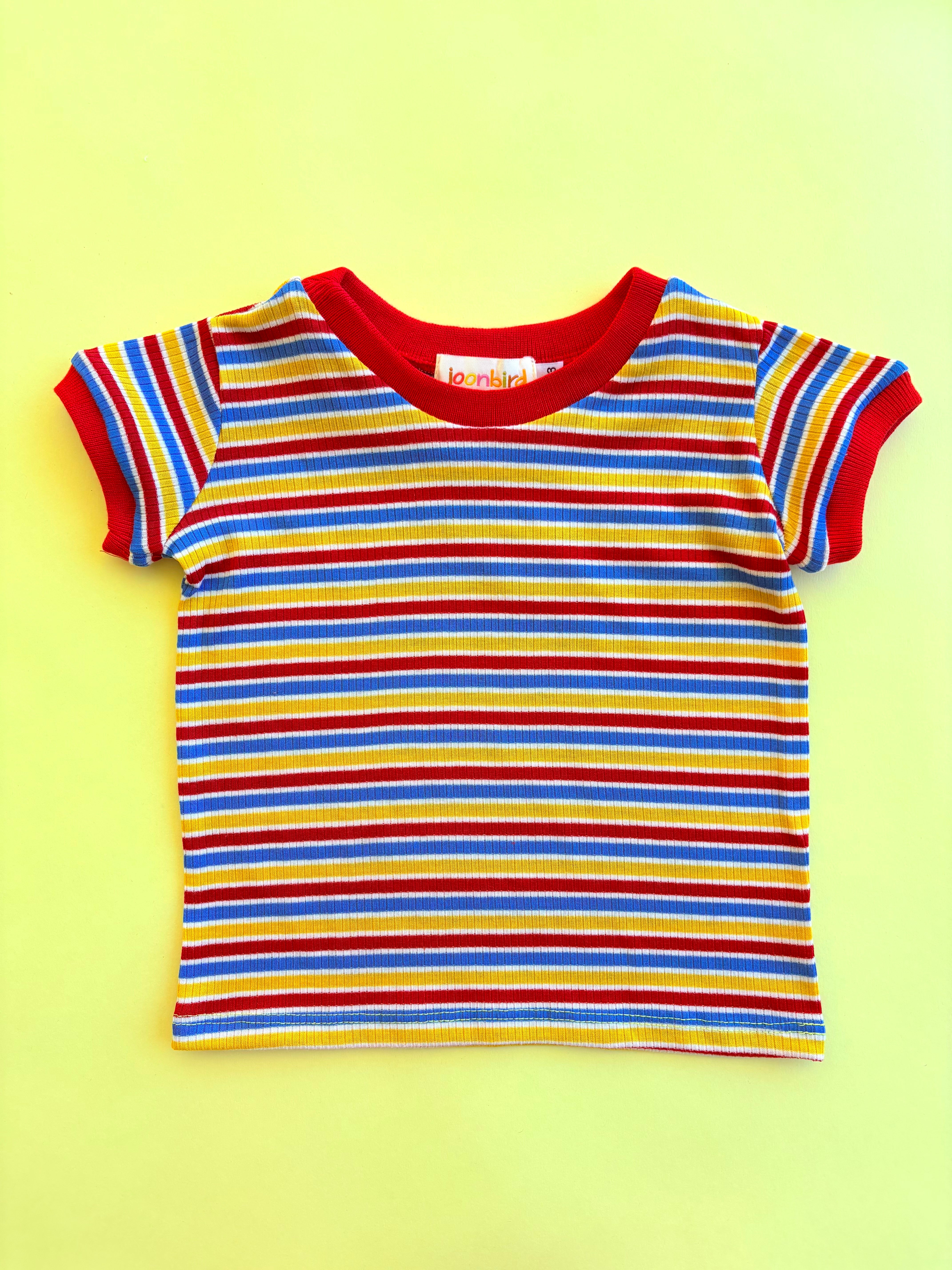 Colorful kids striped shirt with red trim on a yellow background