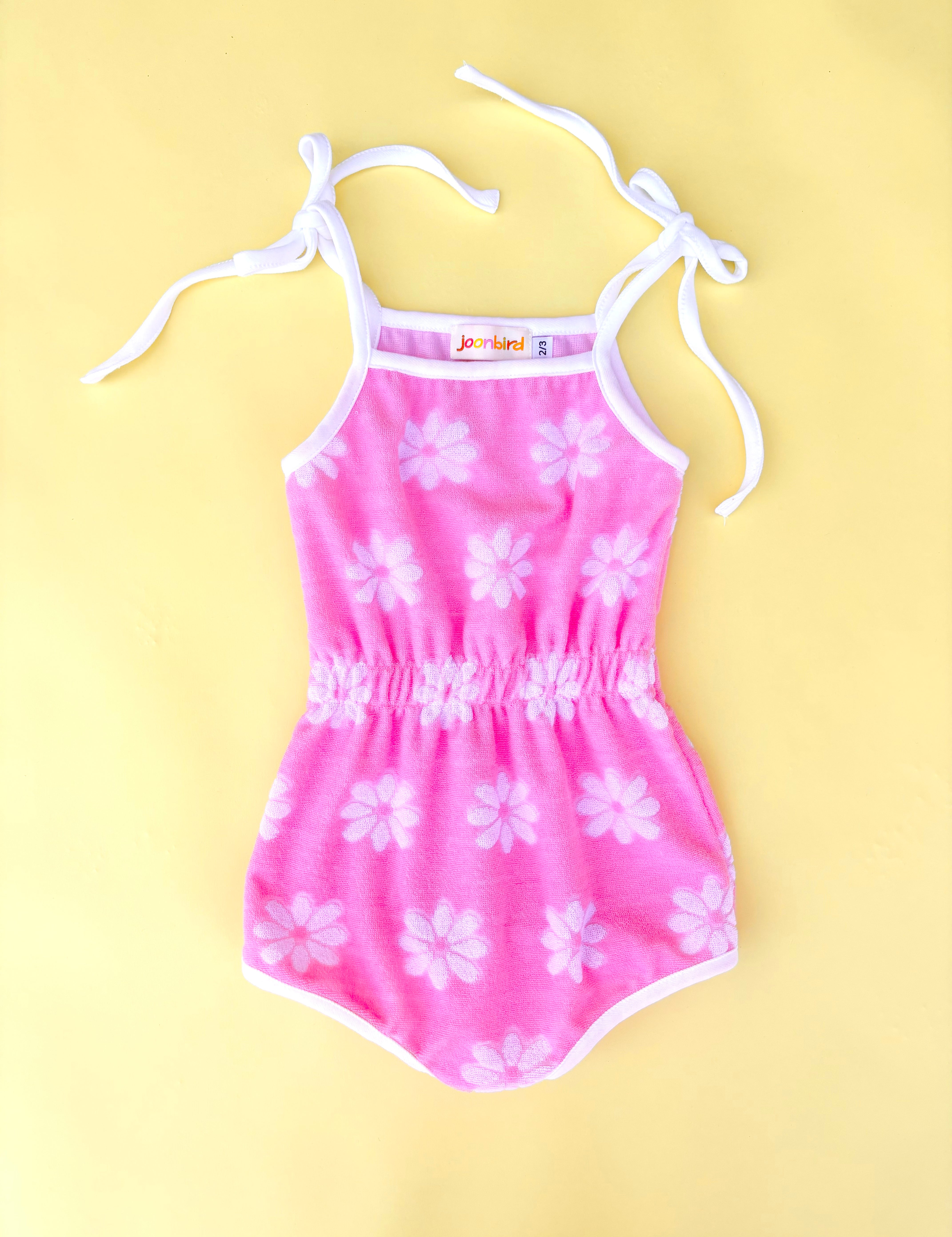 Pink floral romper with white straps on a yellow background