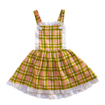 Green and pink plaid girls pinafore dress with white lace trim on a white background