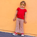 Child wearing a red shirt and checkered bell bottom pants against an orange wall