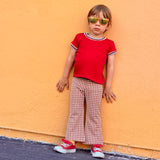 Child wearing a red shirt and checkered bell bottom pants against an orange wall
